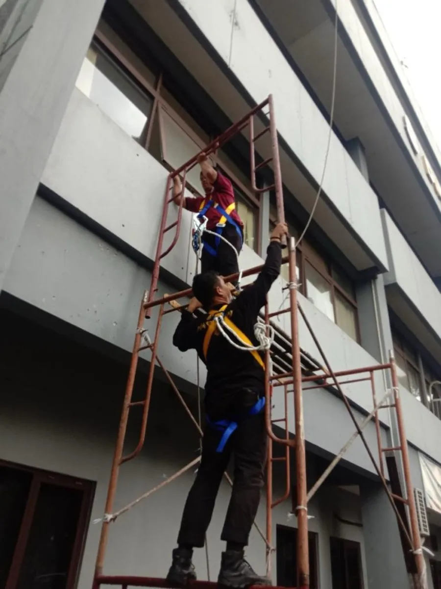 Petugas membersihkan fasad gedung dari perancah